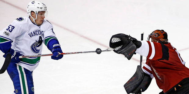 Arizona Coyotes goalie Mike Smith, right, reaches out to grab the puck before Vancouver Canucks cen...