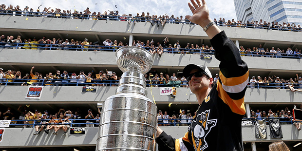 Pittsburgh Penguins' Sidney Crosby waves to the crowd while holding onto the Stanley Cup while ridi...