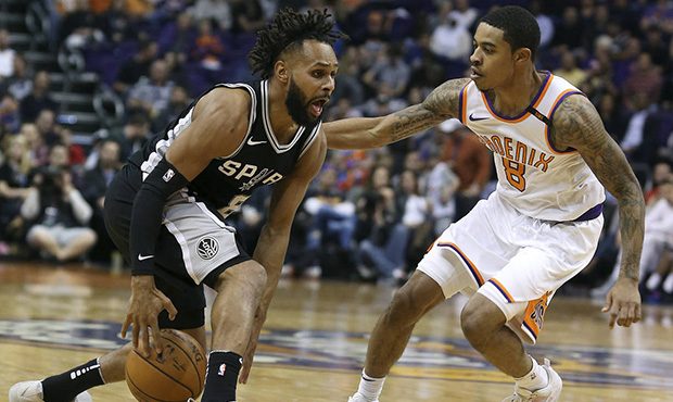 San Antonio Spurs guard Patty Mills, left, dribbles the ball between his legs as Phoenix Suns' Tyle...