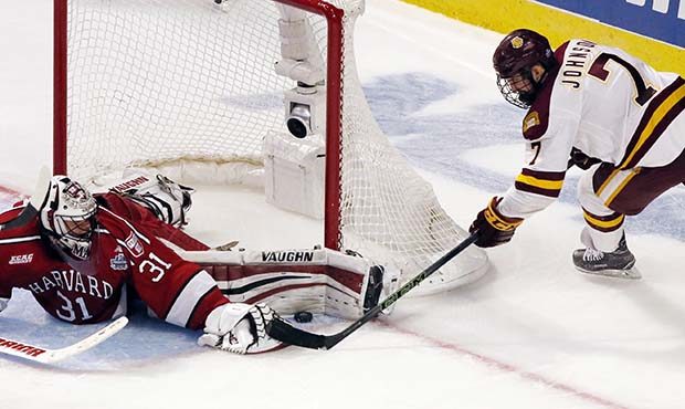 Harvard goalie Merrick Madsen, left, blocks a shot by Minnesota-Duluth center Adam Johnson during t...