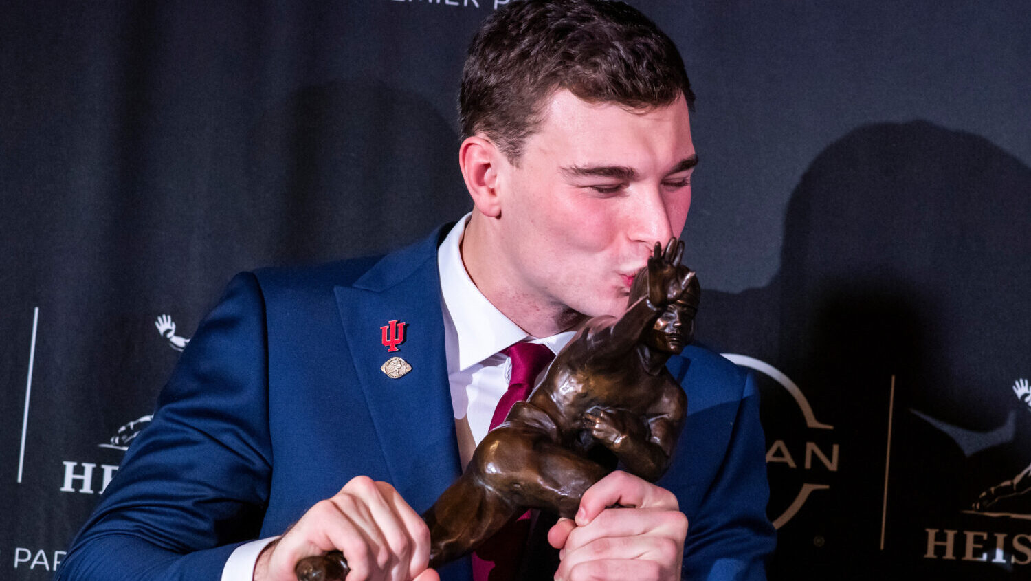 Indiana quarterback Fernando Mendoza kisses the Heisman Trophy...