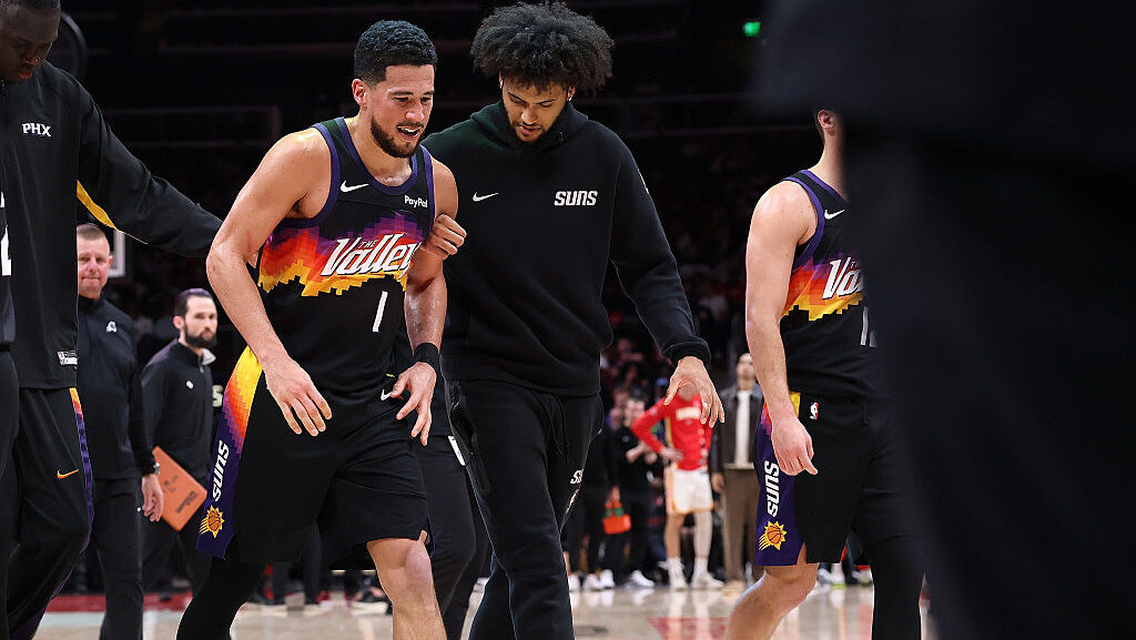 ATLANTA, GEORGIA - JANUARY 23: Devin Booker #1 of the Phoenix Suns is helped off the court after an...